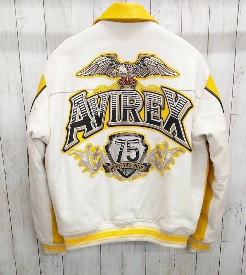 May include: White leather jacket with yellow detailing, featuring the word "AVIREX" in large lettering on the back. An eagle emblem and the text "75 AVIATOR'S KING" are also visible.