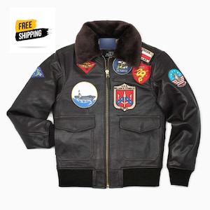 Pode incluir: Jaqueta bomber de couro preto com gola de pele sintética e vários patches bordados, incluindo um navio, um dragão e um emblema da Marinha dos EUA.