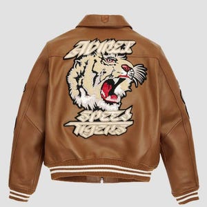 May include: Brown leather bomber jacket with a tiger graphic on the back. The jacket features a white and brown striped collar and cuffs. The tiger graphic includes the words "ADRENALINE" and "SPEED TIGERS".