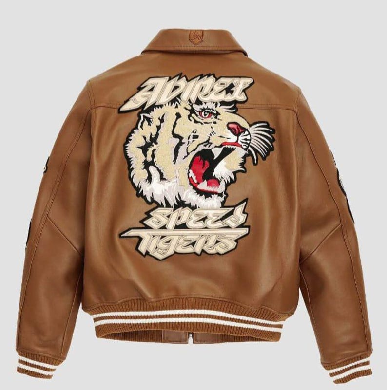 May include: Brown leather bomber jacket with a tiger graphic on the back. The jacket features a white and brown striped collar and cuffs. The tiger graphic includes the words "ADRENALINE" and "SPEED TIGERS".