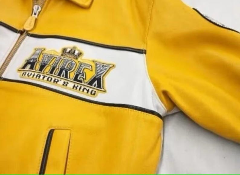 May include: Yellow leather jacket with white stripe detail and the text "AVIREX AVIATOR'S KING" on the chest. Features a zipper closure and a small pocket. The jacket has a classic, sporty design.