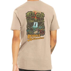 May include: A tan t-shirt with a graphic print of a waterfall in a forest. The graphic also includes the text "Protect Hellbenders" and "Don't Move Rocks".