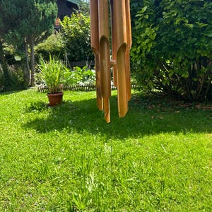 以下が含まれることがあります： 芝生の庭にぶら下がっている茶色の竹製の風鈴。風鈴は木製のトップと、長さの異なる複数のチューブを持っています。