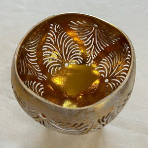 May include: A gold coconut bowl with a carved design of leaves. The bowl is made from a natural coconut shell and has a shiny, metallic finish.