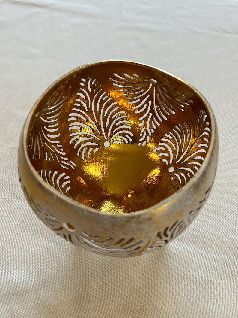 May include: A gold coconut bowl with a carved design of leaves. The bowl is made from a natural coconut shell and has a shiny, metallic finish.