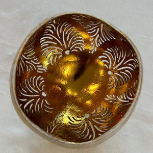 May include: A gold coconut bowl with a decorative carved design. The bowl is made from a natural coconut shell and has a smooth, polished finish.
