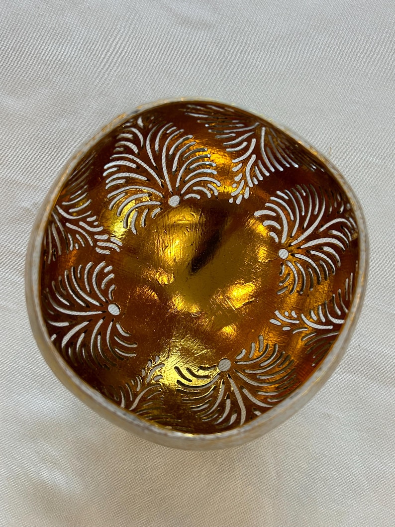 May include: A gold coconut bowl with a decorative carved design. The bowl is made from a natural coconut shell and has a smooth, polished finish.