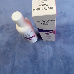 Puede incluir: Una botella y una caja blancas de loción de alquitrán de hulla. La botella está en ángulo, mostrando el nombre del producto y una tapa blanca. La caja es blanca con detalles en rosa y morado, mostrando también el nombre del producto y la marca "SALVE".