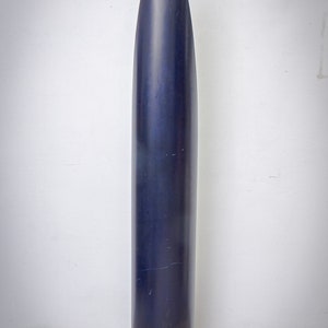 May include: A tall, dark blue, cylindrical object with a pointed top. The object is standing upright against a white wall and a tiled floor. The surface of the object appears smooth with some minor imperfections.