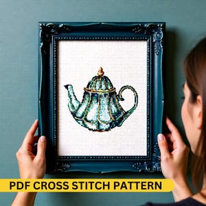 May include: A framed cross-stitch pattern of a teal teapot with gold accents. The teapot is centered on a white background and framed in a dark teal ornate frame. The text "PDF CROSS STITCH PATTERN" is displayed at the bottom.