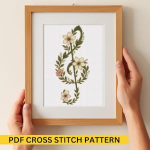 May include: A framed cross-stitch pattern featuring a floral treble clef design. The clef is composed of green leaves and adorned with cream and pink flowers. The frame is light brown, and the text "PDF CROSS STITCH PATTERN" is at the bottom.