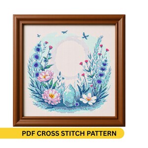 Puede incluir: Un patrón de punto de cruz enmarcado con un diseño floral. Presenta flores rosas y azules, hojas turquesas y un cristal central. El marco es marrón y el texto "PDF CROSS STITCH PATTERN" está en la parte inferior.