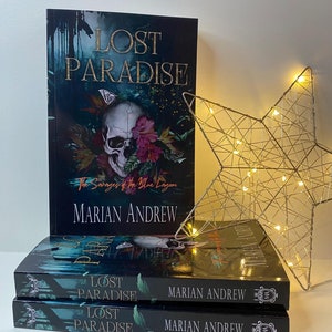 May include: Three paperback books stacked on top of each other. The top book is titled "Lost Paradise" with the subtitle "The Savages of the Blue Lagoon" and the author's name "Marian Andrew". The bottom two books are titled "Lost Paradise" with the author's name "Marian Andrew".