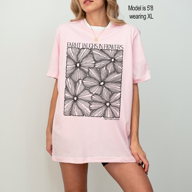 May include: Pink oversized t-shirt with a black graphic of stylized flowers and the text "Farht Laughs in Flowers".