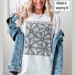 May include: A gray t-shirt with a black and white graphic of stylized flowers. The text "FARHT LAUGHS IN FLOWER" is printed on the shirt. The text "High Wilde Emerson" is printed below the graphic.