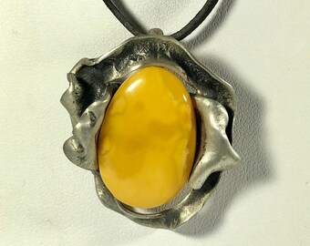 May include: A silver pendant necklace with a large, oval-shaped amber stone set in a textured silver frame. The necklace has a black cord.