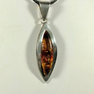 May include: A silver pendant necklace with a teardrop-shaped amber stone set in a silver frame. The necklace is on a black cord.
