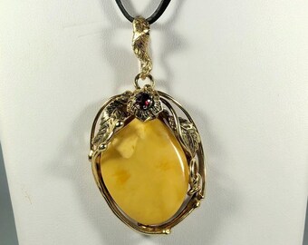May include: A gold pendant necklace with a large oval amber stone set in a gold leaf design. A small red gemstone is set in the center of the leaves.
