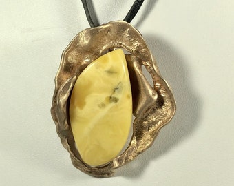 May include: A gold pendant necklace with a large, teardrop-shaped amber stone set in a textured, abstract metal frame. The necklace is on a black leather cord.