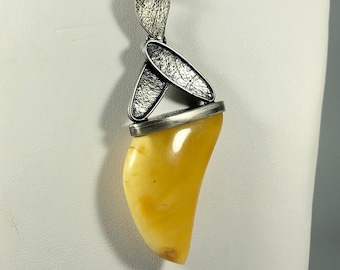May include: A silver pendant with a textured surface and a large amber teardrop-shaped stone. The pendant is attached to a black leather cord.