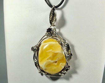 May include: A silver pendant with a large amber stone set in a delicate silver floral design. The pendant is accented with small red gemstones and hangs from a black cord.