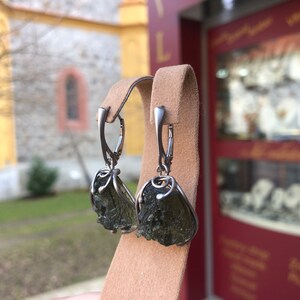 May include: A pair of silver earrings with green aventurine stones. The stones are rough and have a natural, unpolished look. The earrings are hanging from a silver hook.