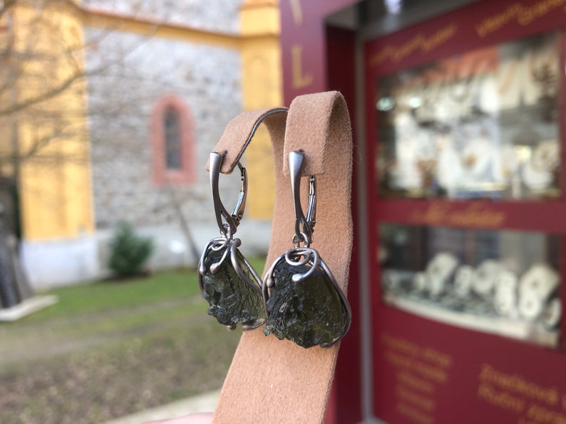 May include: A pair of silver earrings with green aventurine stones. The stones are rough and have a natural, unpolished look. The earrings are hanging from a silver hook.