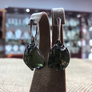 May include: A pair of silver earrings with green gemstone drops. The gemstones are irregularly shaped and have a rough, natural texture.