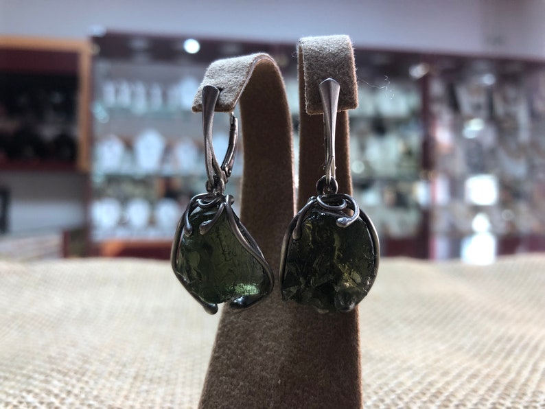 May include: A pair of silver earrings with green gemstone drops. The gemstones are irregularly shaped and have a rough, natural texture.