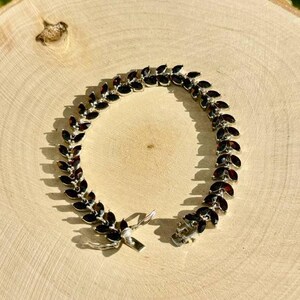 May include: A silver bracelet featuring a row of dark red marquise-shaped gemstones. The bracelet has a clasp fastening.