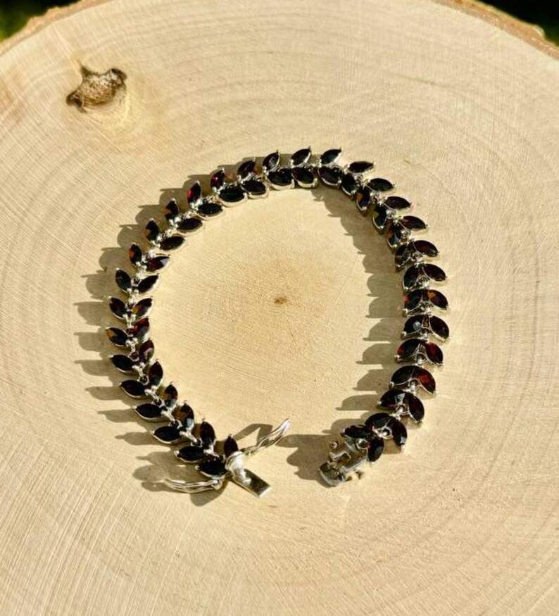 May include: A silver bracelet featuring a row of dark red marquise-shaped gemstones. The bracelet has a clasp fastening.