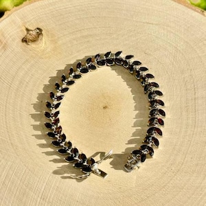 May include: A silver bracelet featuring a row of dark red gemstones set in a leaf-like design.
