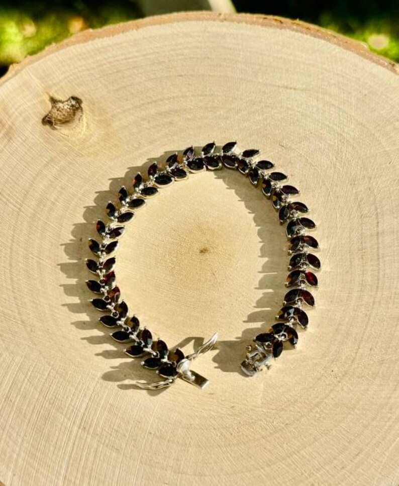 May include: A silver bracelet featuring a row of dark red gemstones set in a leaf-like design.