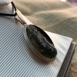 May include: A silver pendant necklace with a round, green and black stone. The stone has a rough, textured surface.