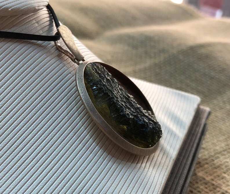 May include: A silver pendant necklace with a round, green and black stone. The stone has a rough, textured surface.