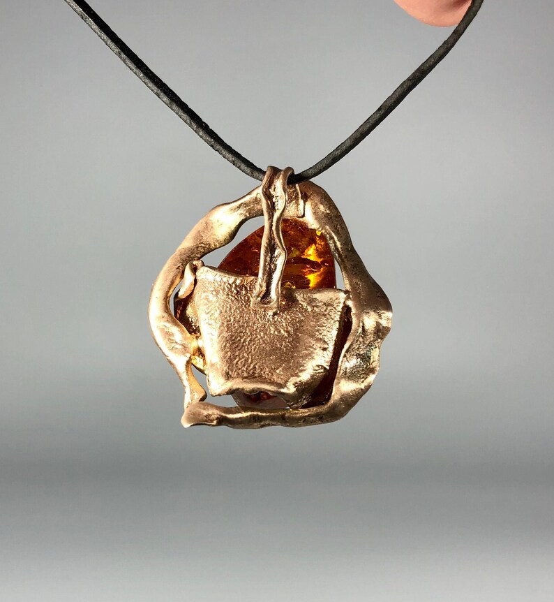May include: A gold pendant necklace with a large amber stone set in a geometric frame. The necklace is on a black cord.
