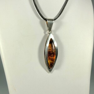 May include: A silver pendant necklace with a teardrop-shaped amber stone set in a silver frame. The necklace is on a black leather cord.