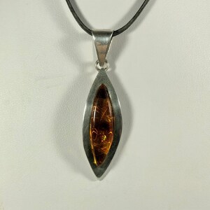 May include: A silver pendant necklace with a teardrop-shaped amber stone set in a silver frame. The necklace is on a black cord.