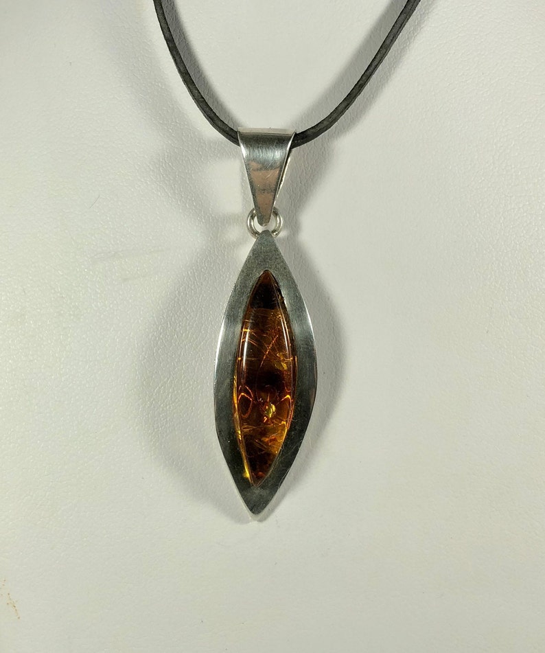 May include: A silver pendant necklace with a teardrop-shaped amber stone set in a silver frame. The necklace is on a black cord.