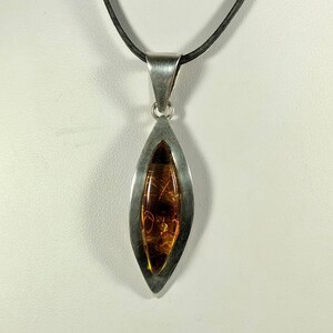 May include: A silver pendant necklace with a teardrop-shaped amber stone. The pendant is set in a silver frame and hangs from a black cord.