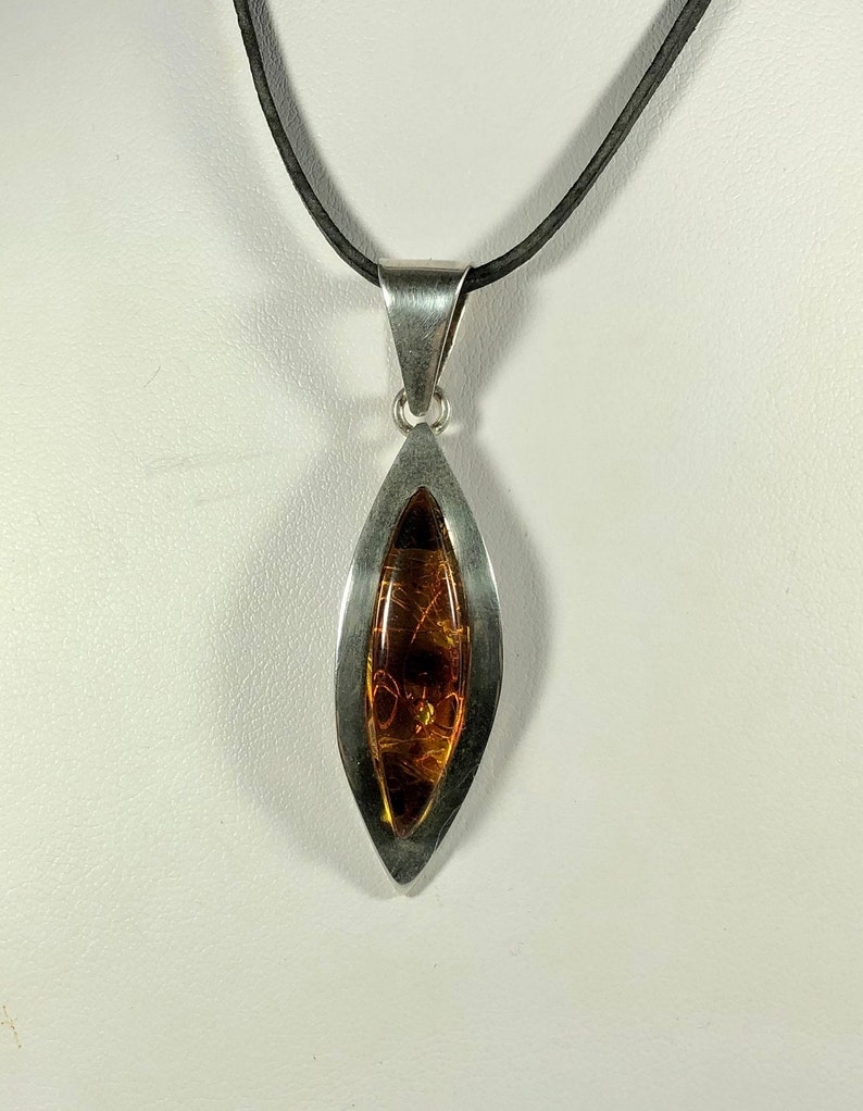 May include: A silver pendant necklace with a teardrop-shaped amber stone. The pendant is set in a silver frame and hangs from a black cord.