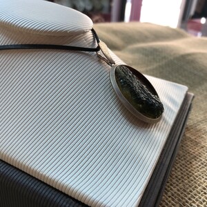 May include: A silver pendant necklace with a round green and black stone. The stone is set in a silver bezel and has a rough, natural texture.
