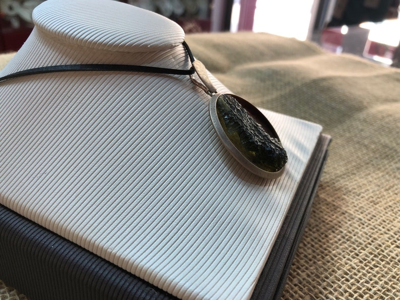 May include: A silver pendant necklace with a round green and black stone. The stone is set in a silver bezel and has a rough, natural texture.