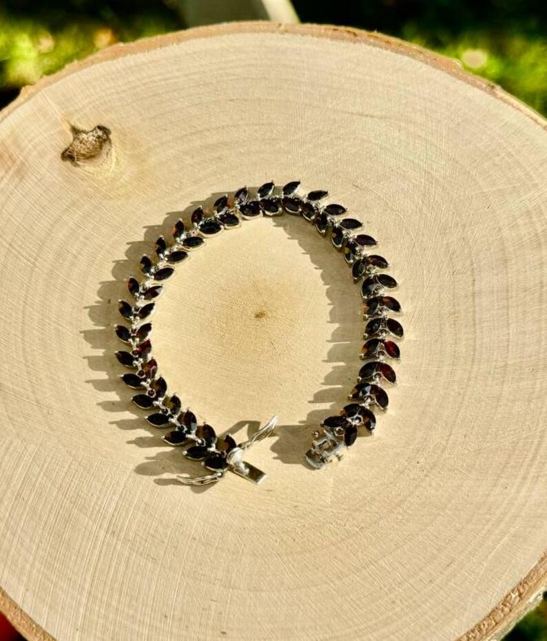 May include: A silver bracelet featuring a row of dark red marquise-shaped stones. The bracelet has a clasp fastening.