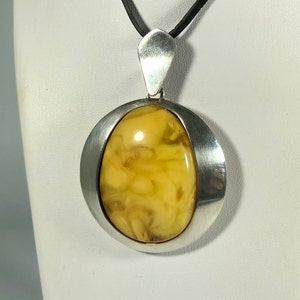 May include: A silver pendant with a large oval amber stone set in a silver frame. The pendant is hanging from a black cord.