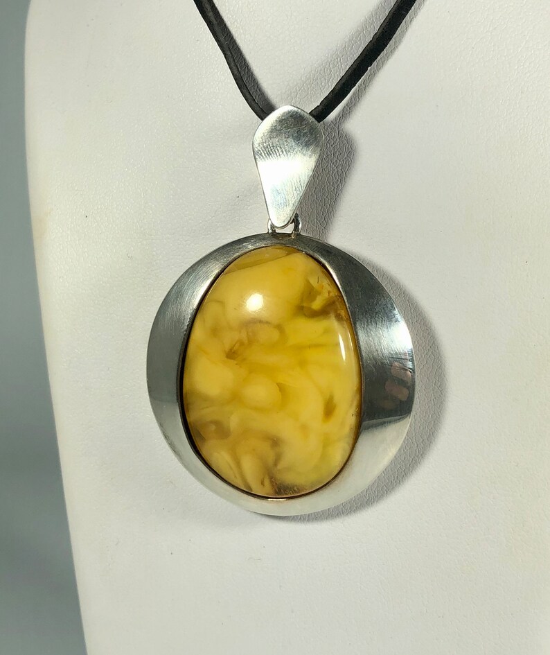 May include: A silver pendant with a large oval amber stone set in a silver frame. The pendant is hanging from a black cord.