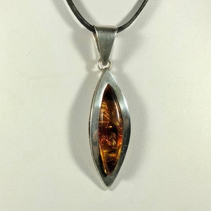 May include: A silver pendant necklace with a teardrop-shaped amber stone set in a silver frame. The necklace has a black leather cord.