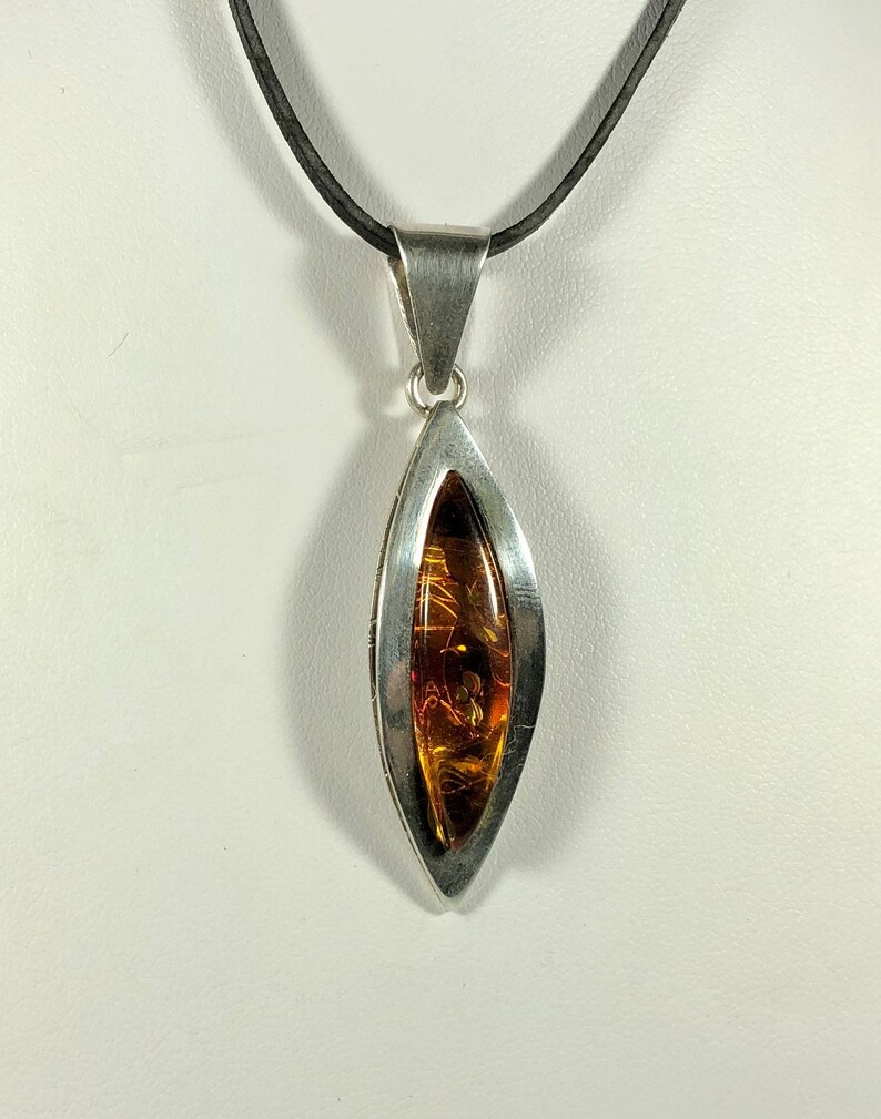 May include: A silver pendant necklace with a teardrop-shaped amber stone set in a silver frame. The necklace has a black leather cord.