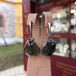 May include: A pair of silver earrings with dark green, rough-cut gemstone drops. The earrings have a simple, elegant design.