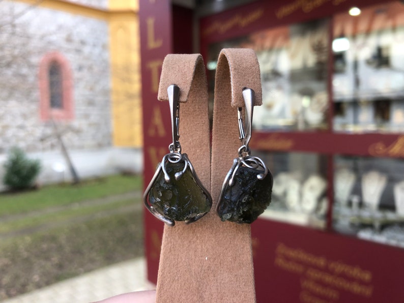 May include: A pair of silver earrings with dark green, rough-cut gemstone drops. The earrings have a simple, elegant design.